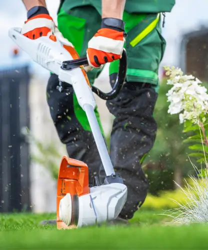 Gartenpflege-Service: Galabauer finalisiert die Rasenkante eines Gartens mit einer Motorsense.