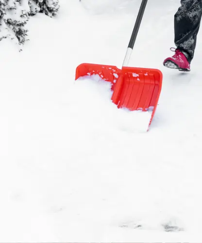 Eine Person räumt Schnee frei, mit einer Schneeschaufel.