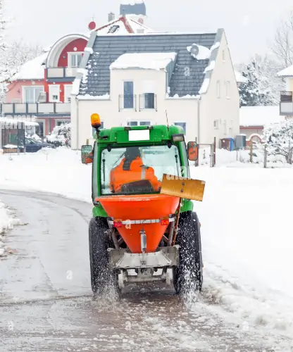 Ein kleiner Traktor umgebaut zu einem Schnee-Räumfahrzeug streut Streusalz auf die frisch geräumte Straße im Winter.